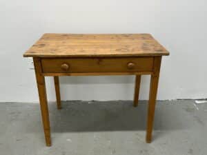 A wooden table with a drawer and round knobs against a plain wall.