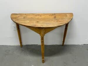 A rustic, half-moon wooden table against a white wall on a concrete floor.