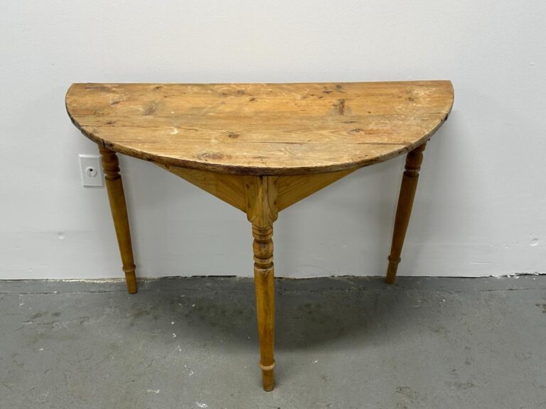 A rustic, half-moon wooden table against a white wall on a concrete floor.