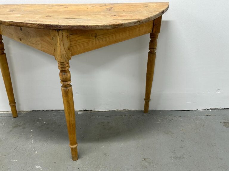 A wooden half-moon table against a white wall on a gray concrete floor.