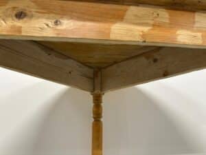 Underneath view of a wooden table corner with one turned leg and visible wood grain patterns.