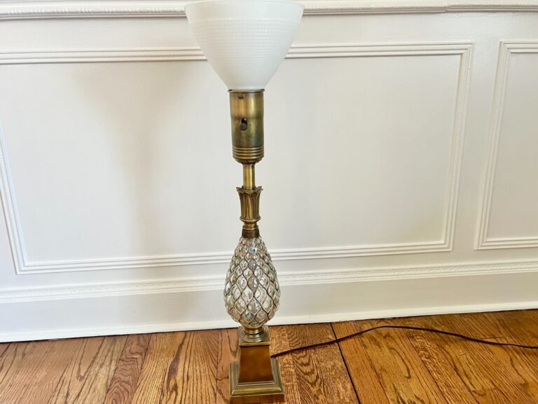 The Vintage Pineapple Crystal & Brass Lamp features ornate glass detailing and a white shade, perfect for a wooden floor.