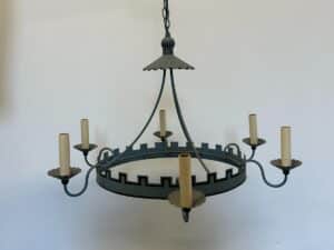 A medieval-style metal chandelier with candle-shaped holders, hanging against a plain background.