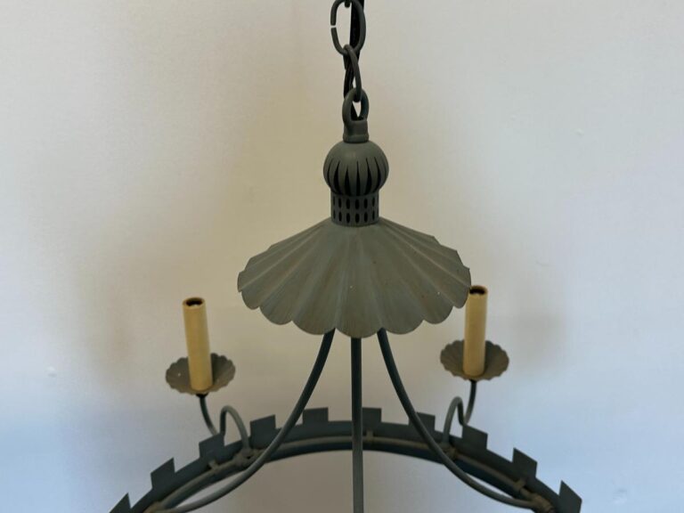 Metal chandelier with a scalloped design and candle-style light holders, hanging against a plain white wall.