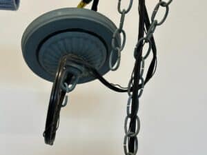 Close-up of a ceiling light fixture with tangled black cords and gray chains against a white background.