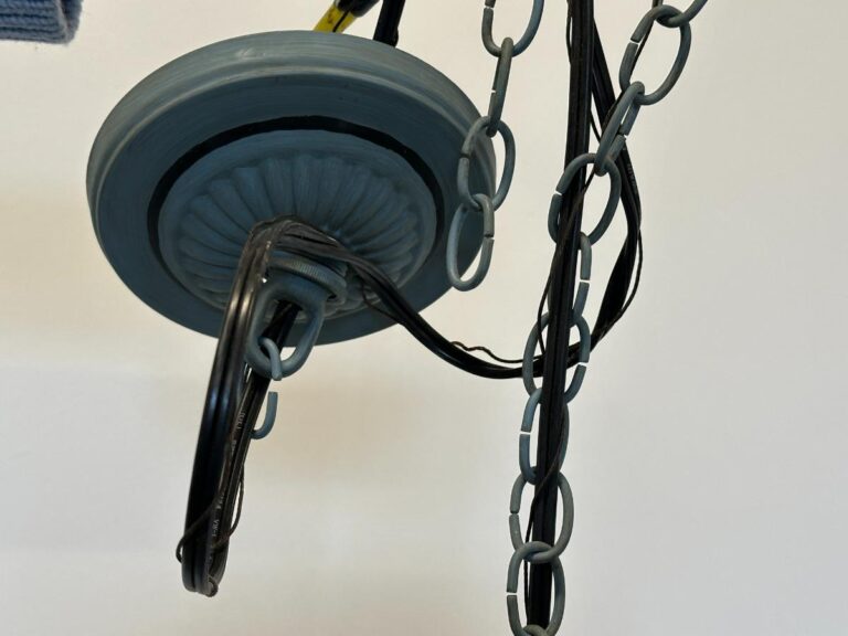Close-up of a ceiling light fixture with tangled black cords and gray chains against a white background.