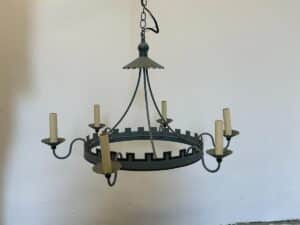 Rustic metal chandelier with castle-like design and candle-style lights against a plain white wall.