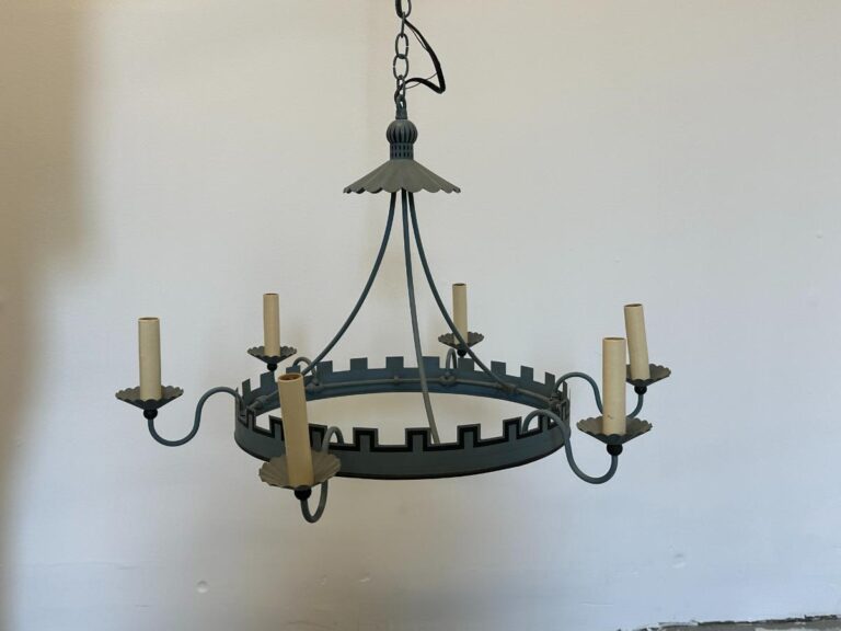 Rustic metal chandelier with castle-like design and candle-style lights against a plain white wall.