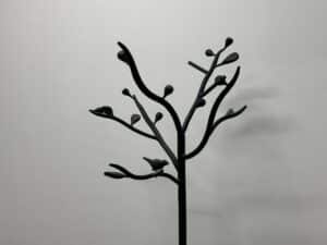 Sculptural coat rack resembling a tree with branches and a bird, set against a plain, light-colored wall.