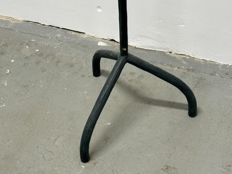 A black three-legged stand on a gray concrete floor beside a white wall.