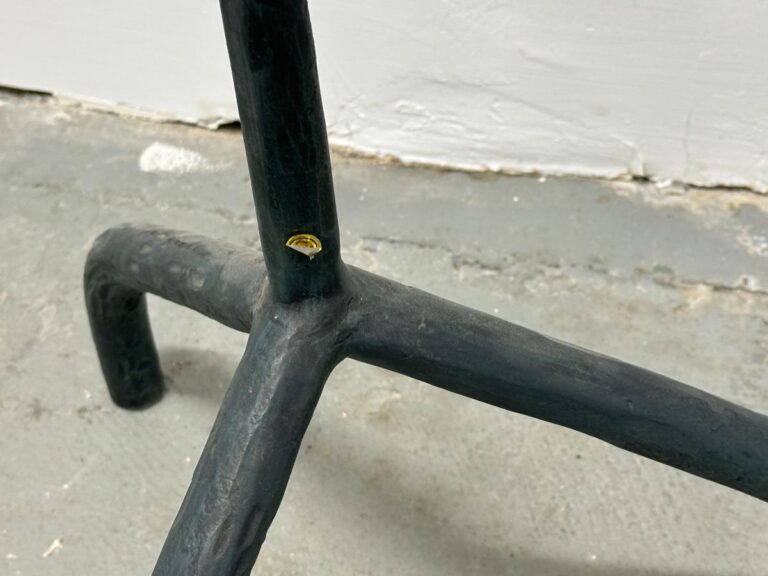 A close-up of a black metal stand with three legs and a small yellow sticker on a gray concrete floor.