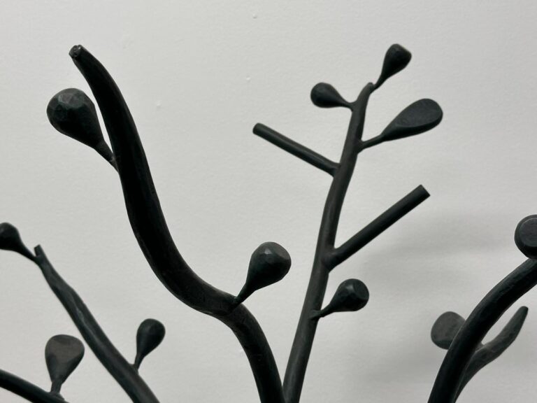 Abstract black metal sculpture resembling tree branches against a plain white background.