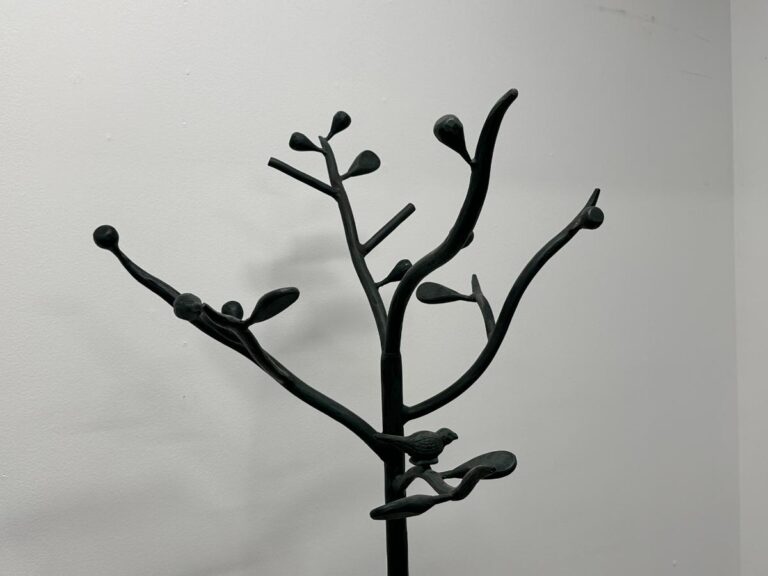 A black metal sculpture of a tree branch with buds against a plain white wall.