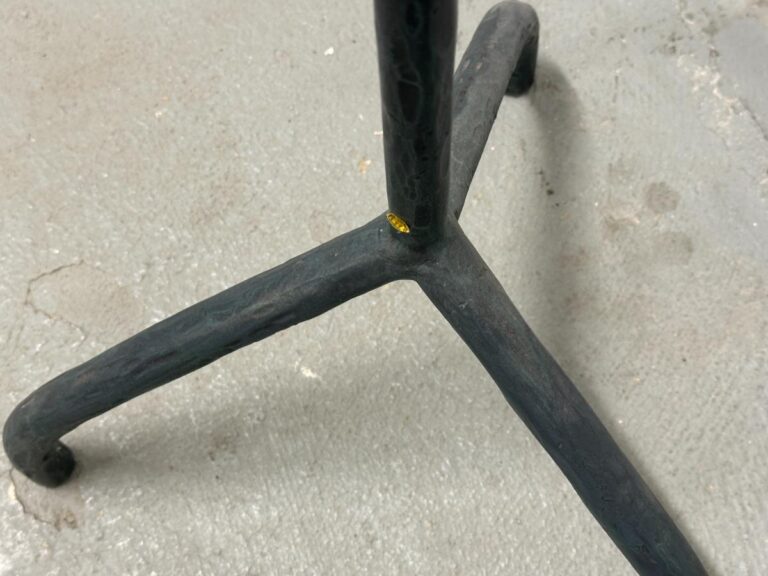 Close-up view of a three-legged black metal stand on a gray concrete floor.