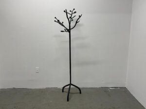 Minimalist coat rack resembling a bare tree, set against a plain white wall and gray floor.