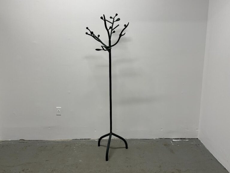 Minimalist coat rack resembling a bare tree, set against a plain white wall and gray floor.