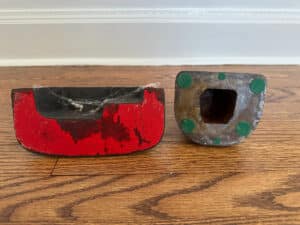 Two "Southern Lady" and "Cape Cod Cottage" door stops in cast iron, painted red and black with green spots, are on a wooden floor.
