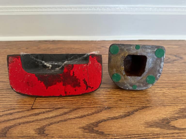 Two "Southern Lady" and "Cape Cod Cottage" door stops in cast iron, painted red and black with green spots, are on a wooden floor.