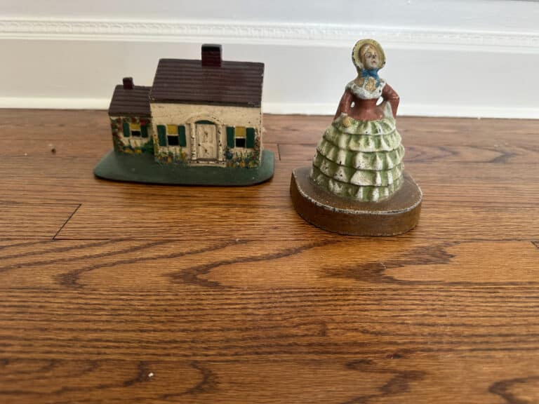 A cast iron painted Southern lady figurine and a Cape Cod cottage door stop on a wooden floor.