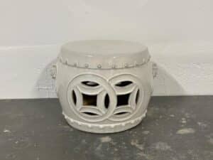 White ceramic stool with intricate cut-out circular patterns, placed on a gray surface against a white wall.