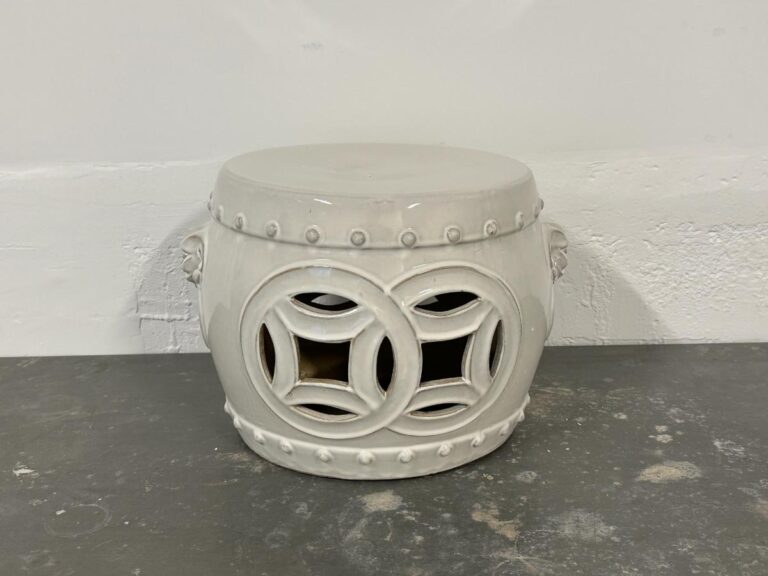 White ceramic stool with intricate cut-out circular patterns, placed on a gray surface against a white wall.