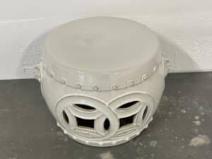 White ceramic garden stool with circular cutout patterns on a gray surface.