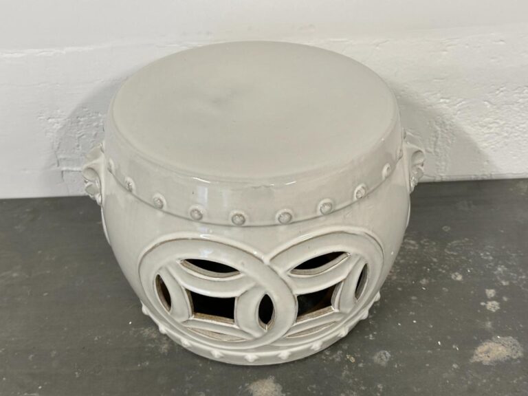 White ceramic garden stool with circular cutout patterns on a gray surface.