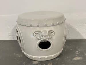 Gray ceramic stool with a face design and round cutouts on the sides, placed on a dark surface.