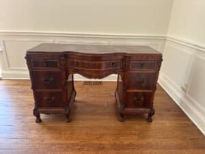 French Carved Mahogany Vanity Ladies Desk with intricate details and multiple drawers sits on a wooden floor against a paneled wall.