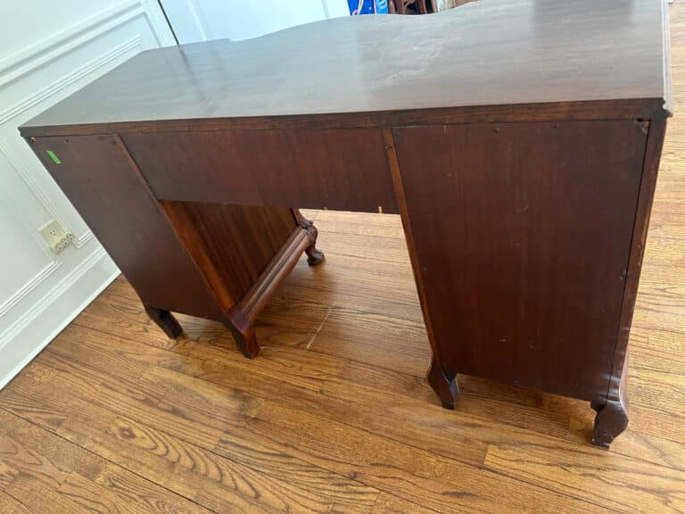The French Carved Mahogany Vanity Ladies Desk, with a dark finish and set on a hardwood floor, has a partially missing front panel.