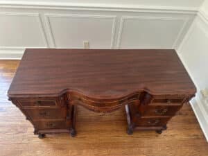 Top view of the French Carved Mahogany Vanity Ladies Desk with decorative carvings and multiple drawers against a white paneled wall.