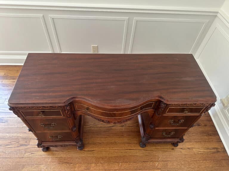 Top view of the French Carved Mahogany Vanity Ladies Desk with decorative carvings and multiple drawers against a white paneled wall.
