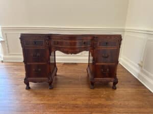 The French Carved Mahogany Vanity Ladies Desk, placed on a hardwood floor, boasts intricate carvings with three central drawers and two side cabinets.