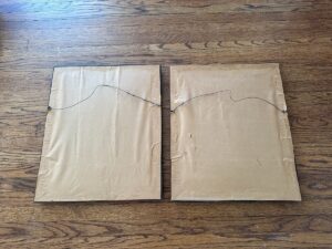 Two "Passé Temps Des Dames" framed prints lie face down on a wooden floor, displaying their hanging wires.