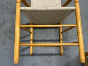 Wooden chair with woven seat, viewed from above, on a gray, textured floor.