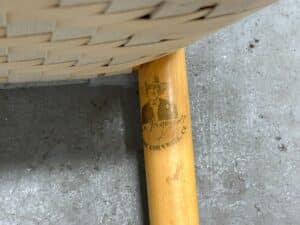 Close-up of a wooden chair leg with a faded logo of a man in a hat and the text "Best Cornwall Chair.