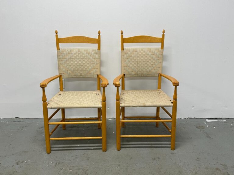 Two wooden chairs with woven seats and backs, positioned side by side against a plain white wall.