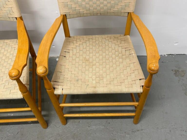 Wooden chair with woven seat and backrest, featuring rounded armrests, next to a similar chair.
