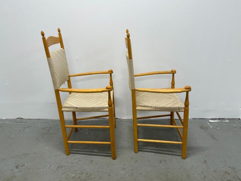 Two wooden chairs with woven seats, side by side against a plain white wall.