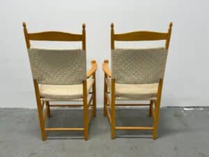 Two wooden chairs with woven backrests and seats, side by side against a plain white wall.