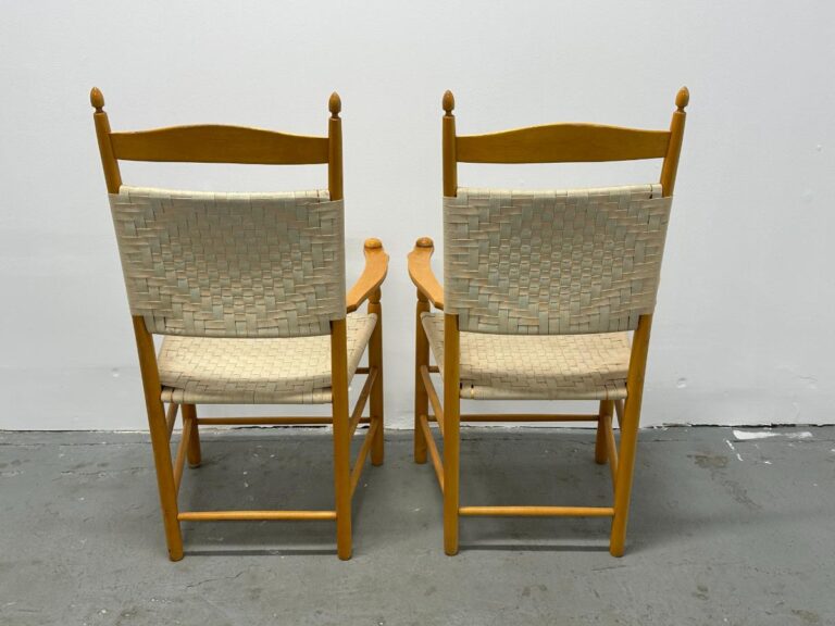 Two wooden chairs with woven backrests and seats, side by side against a plain white wall.