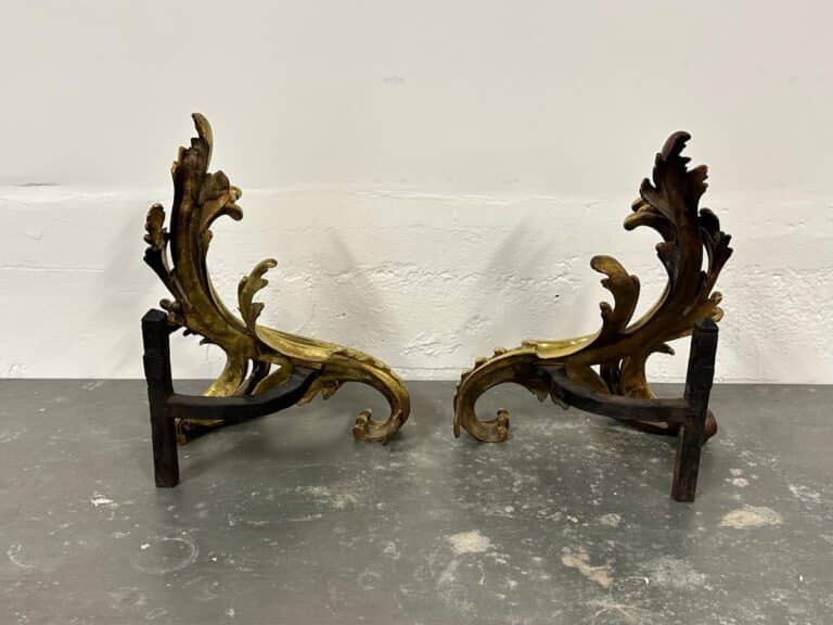 Two ornately carved brass-colored brackets with leaf-like designs on a gray surface.