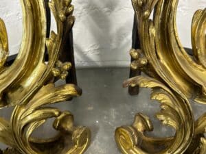 Ornate, gold-colored, leafy metal scrollwork with a textured gray background.