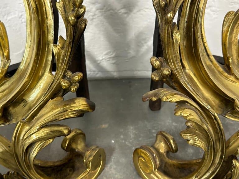 Ornate, gold-colored, leafy metal scrollwork with a textured gray background.