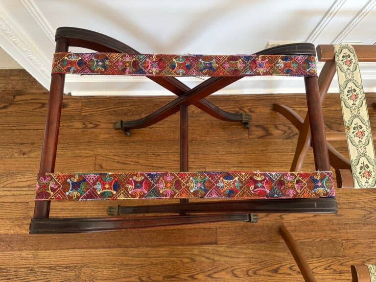 The French Carved Mahogany Vanity Ladies Desk features colorful, patterned fabric straps over a hardwood floor background.