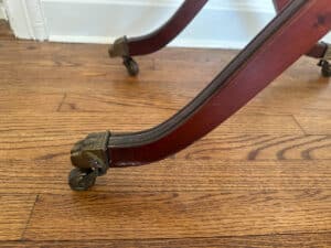 Close-up of the French Carved Mahogany Vanity Ladies Desk's wooden leg featuring a claw foot design and caster wheel on a hardwood floor.