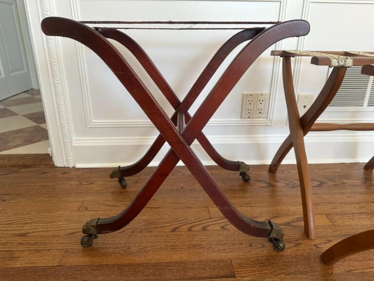 A French Carved Mahogany Vanity Ladies Desk with crossed legs and wheels on a wooden floor, near a wall with outlets.