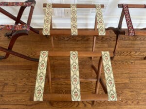 A set of three Antique Regency, Vintage Scheibe, and Reeded Leg luggage racks with patterned fabric straps rests on a wooden floor.