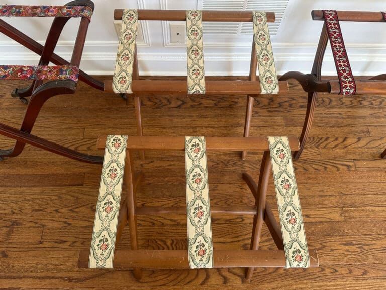 A set of three Antique Regency, Vintage Scheibe, and Reeded Leg luggage racks with patterned fabric straps rests on a wooden floor.