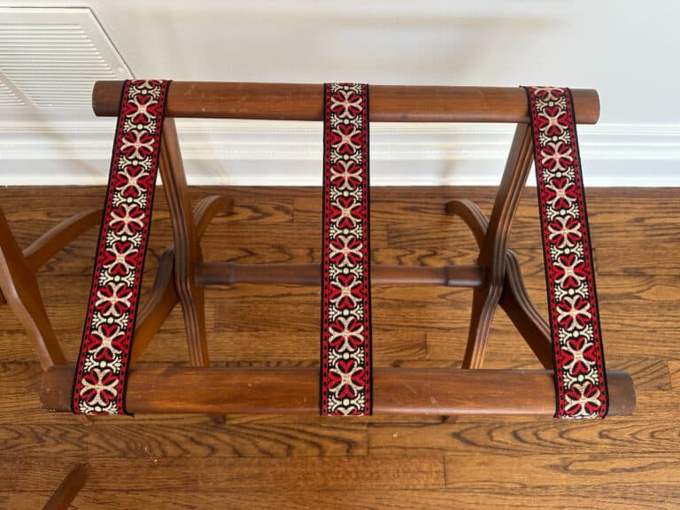 French Carved Mahogany Vanity Ladies Desk on a wooden floor with red and black patterned fabric straps.